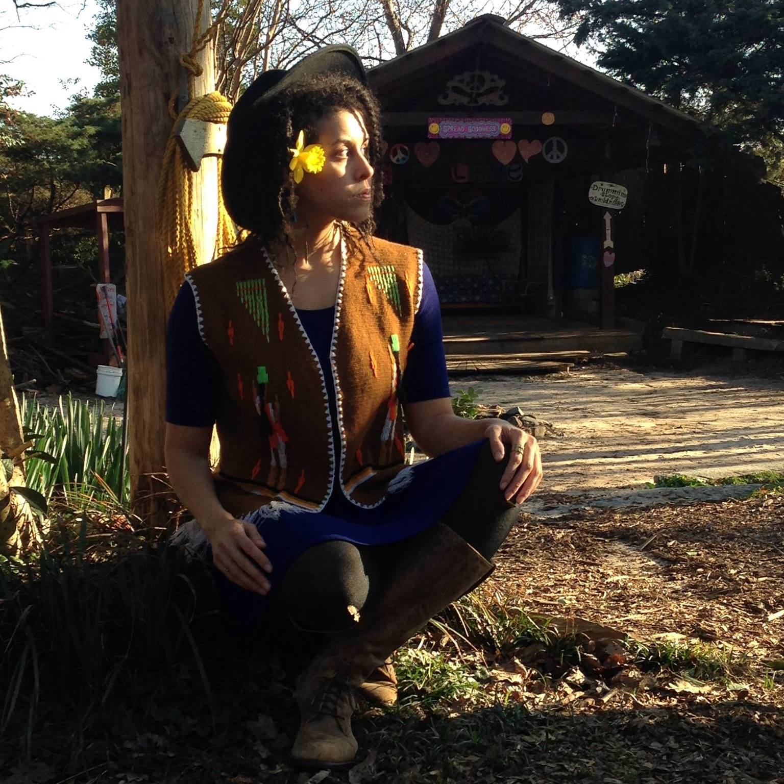 Dawn Mott sitting under a tree in a vintage, handmade tan vest and looking off into the sunset.